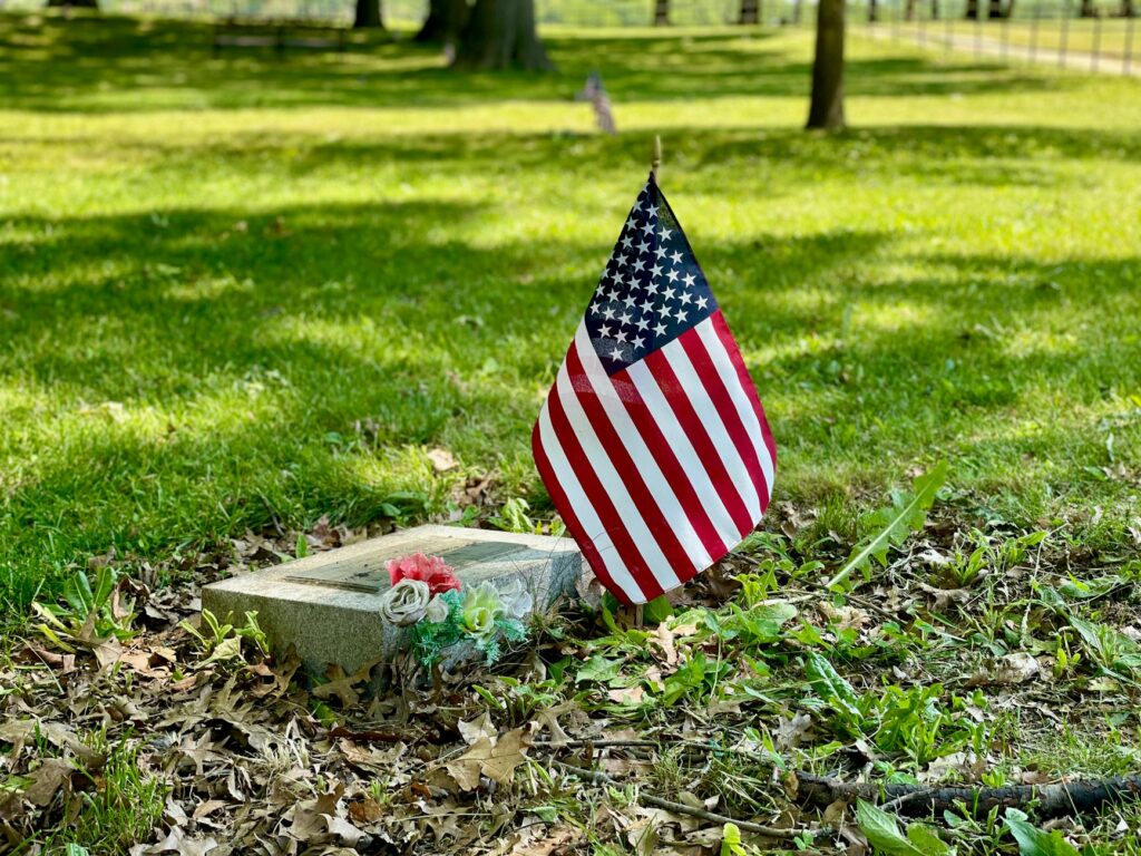 Small American flag at the base of a memorial tree during Memorial Day weekend