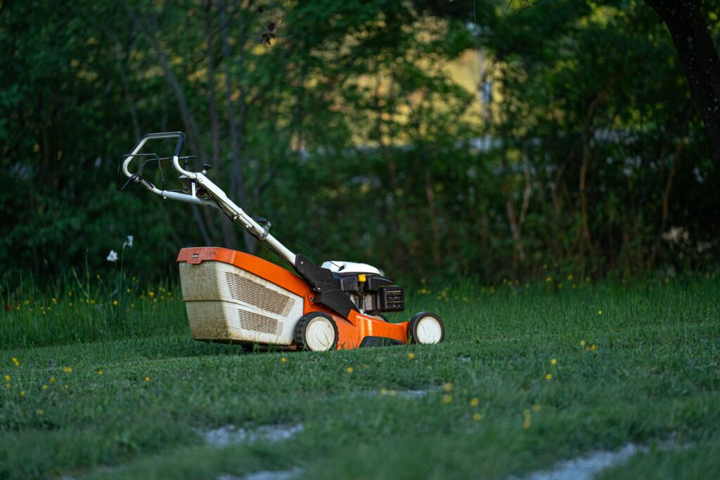 Lawn mower passing close to the base of a mature tree trunk in a suburban yard