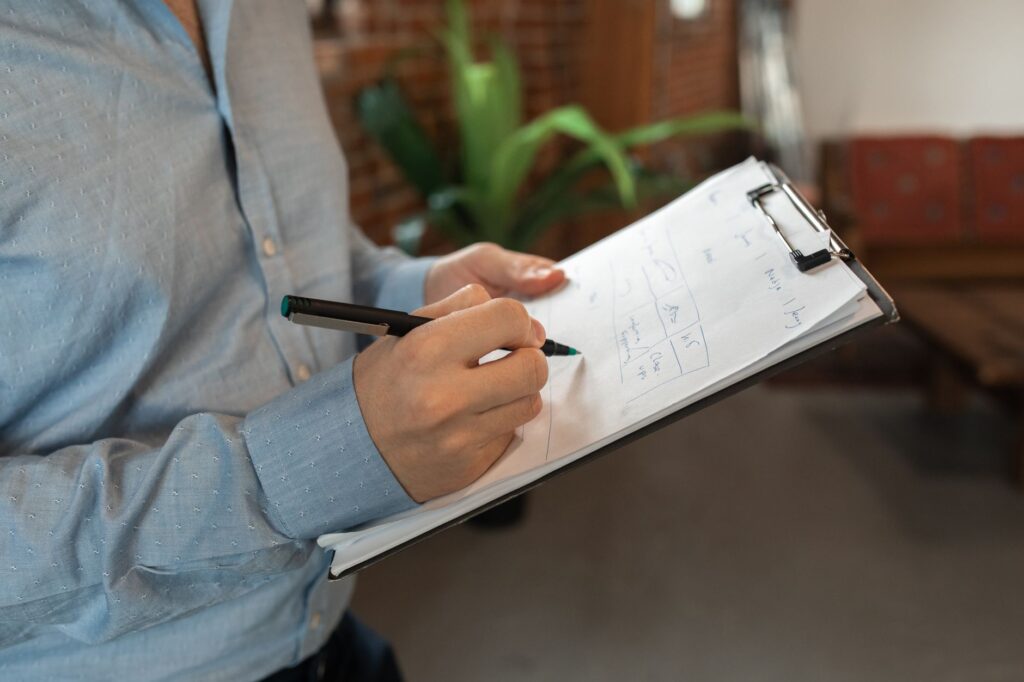 Arborist writing a tree assessment report on a clipboard beside a mature tree