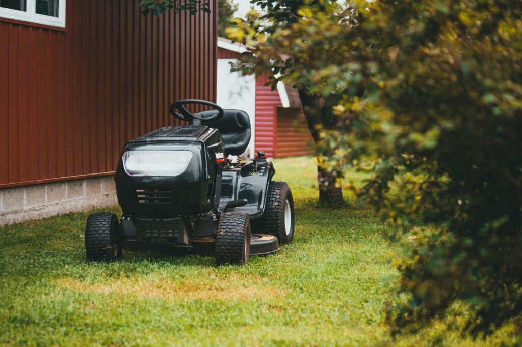 Riding lawn mower passing close to a large tree trunk in a residential backyard