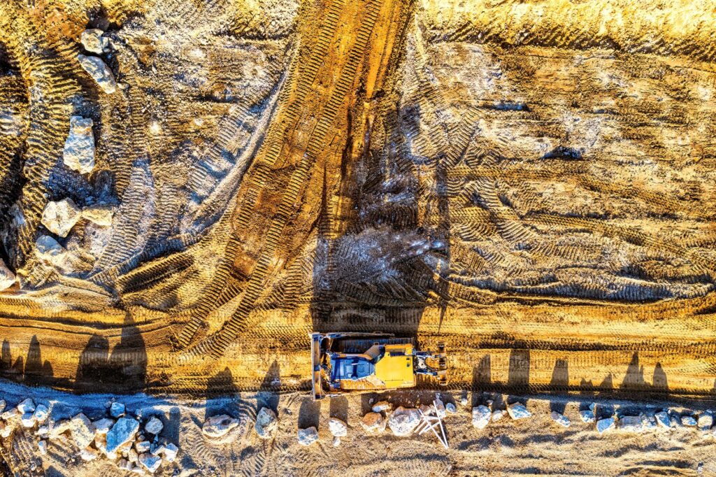 An excavator pulling a full tree root ball from the ground during a complete stump removal
