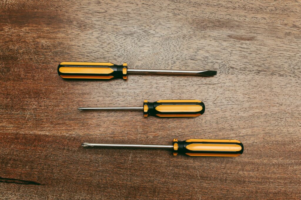 A flathead screwdriver being pushed into soil near a tree's root zone to test moisture